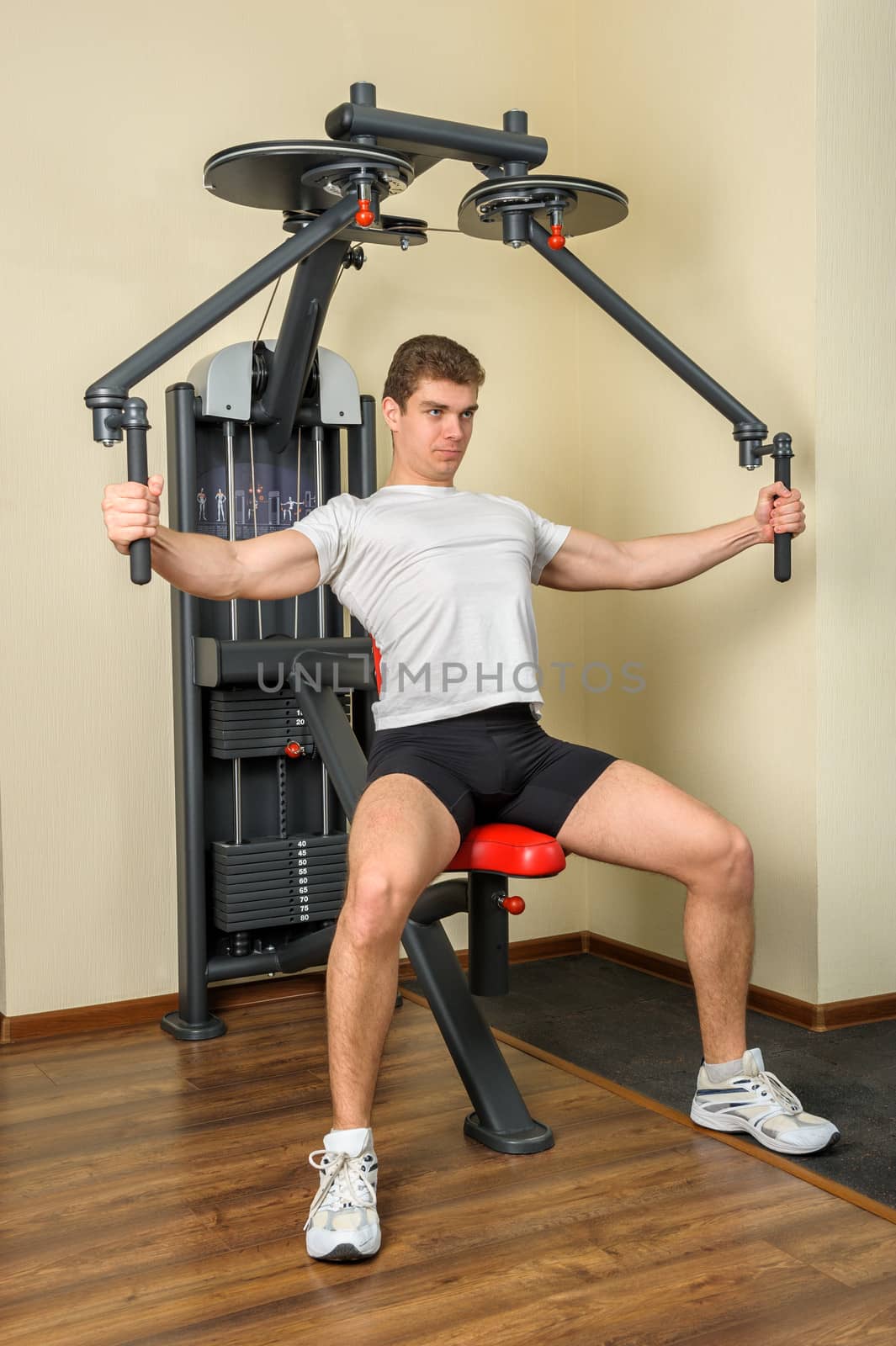 handsome young man does workout at chest fly machine in gym