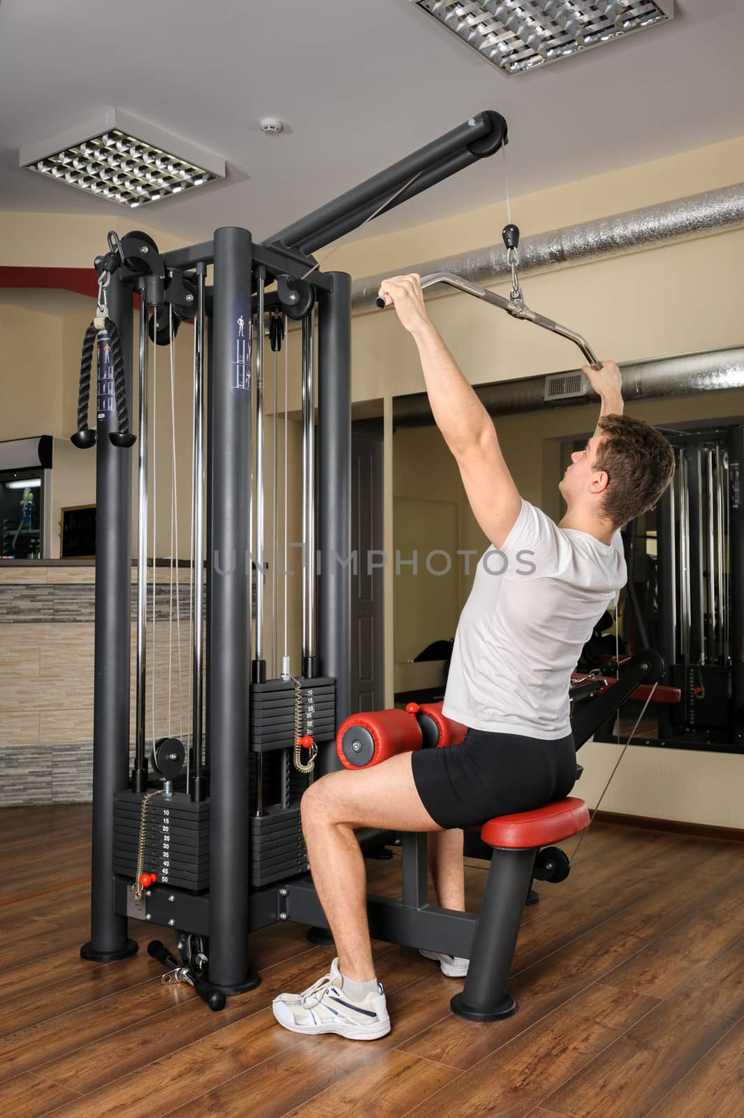 Young man doing lats pull-down workout in gym by starush