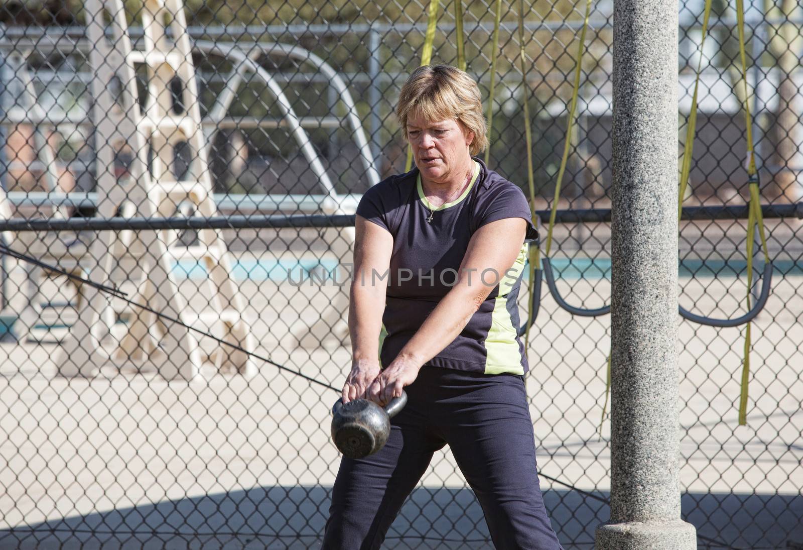 Middle aged woman lifting kettle bell weights outdoors