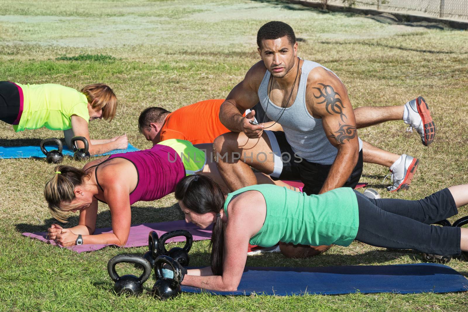 Instructor with tattoo helping bootcamp fitness students