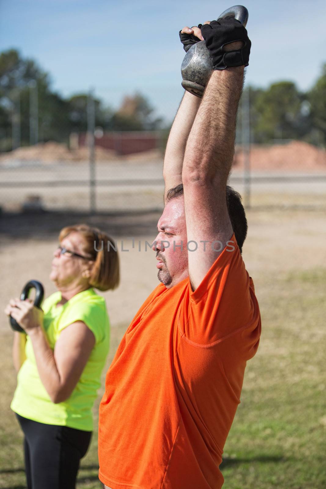 Pair of fit mature adults lifting weights outdoors