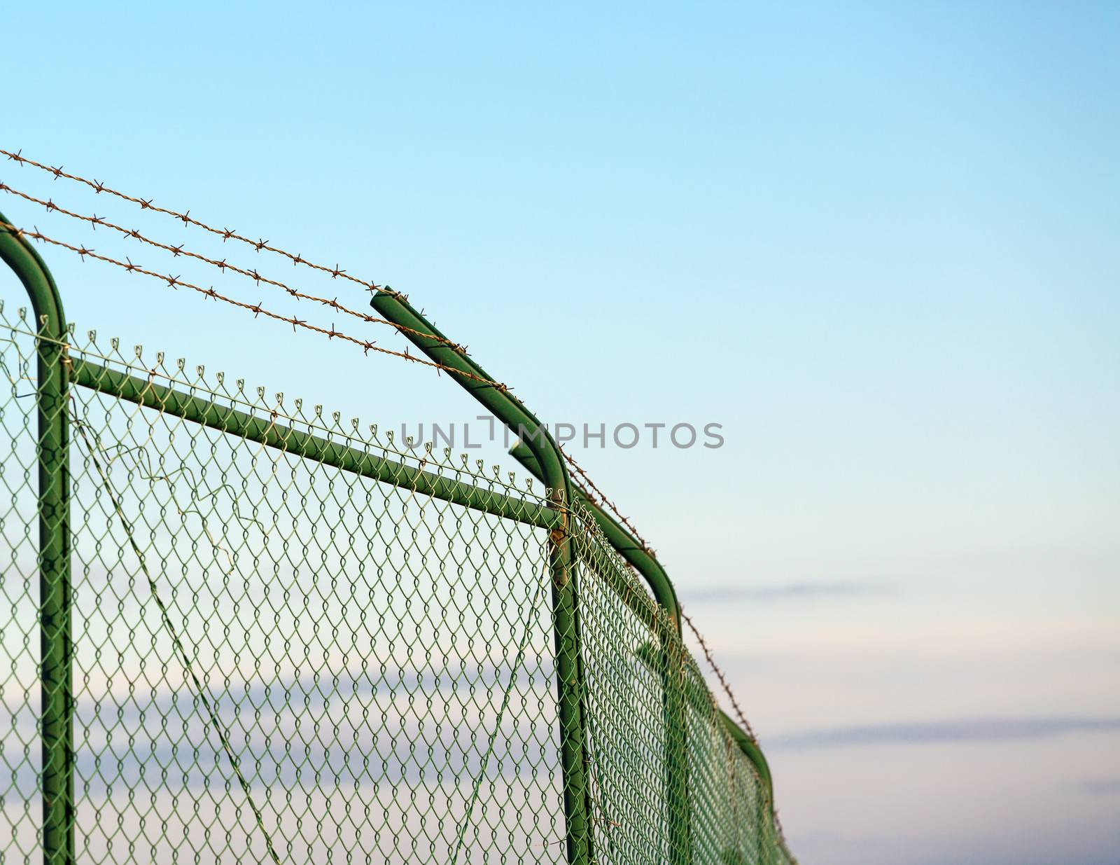 Mesh fence with barbed wire on a background of blue sky