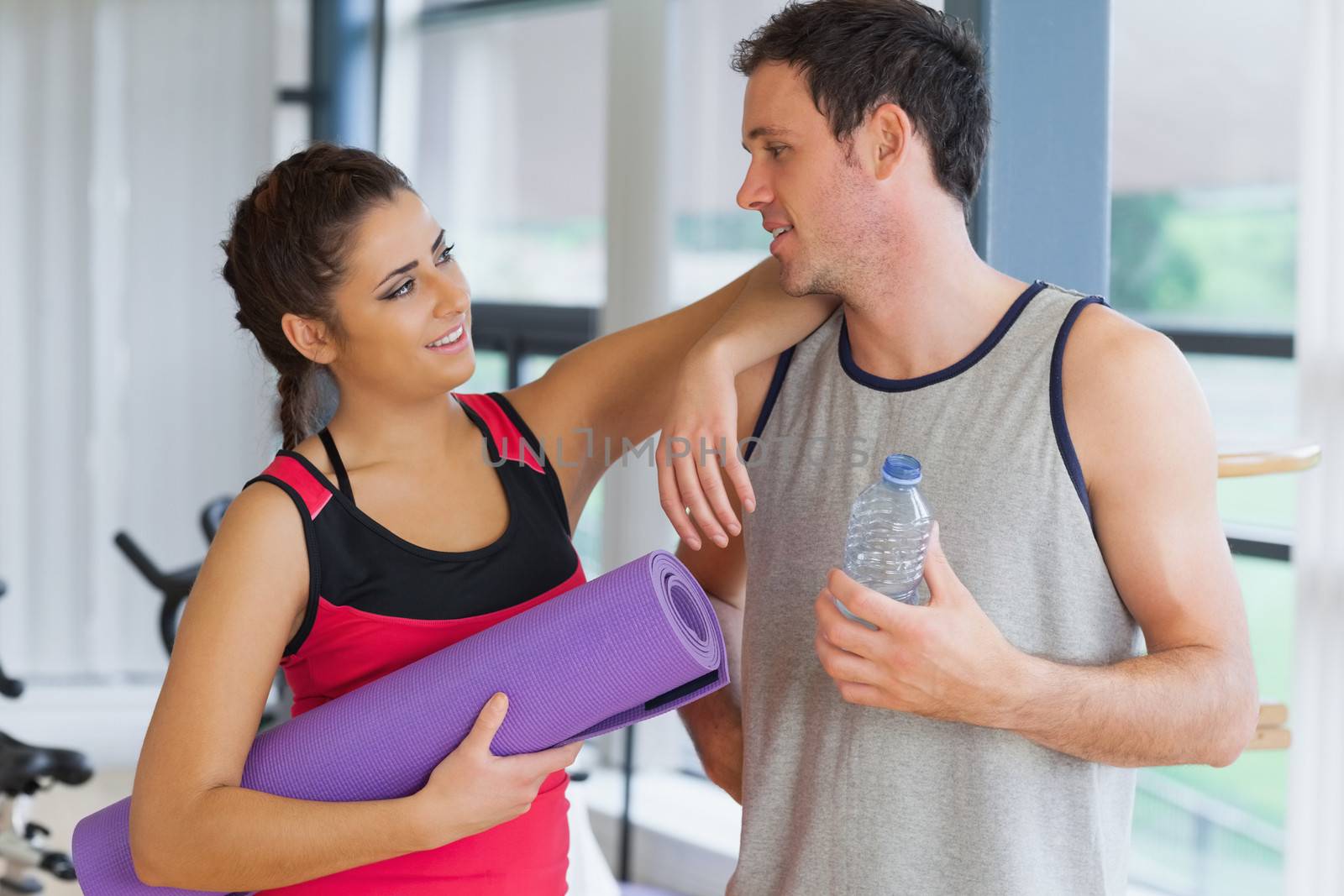 Fit young couple with water bottle and exercise mat in a bright exercise room