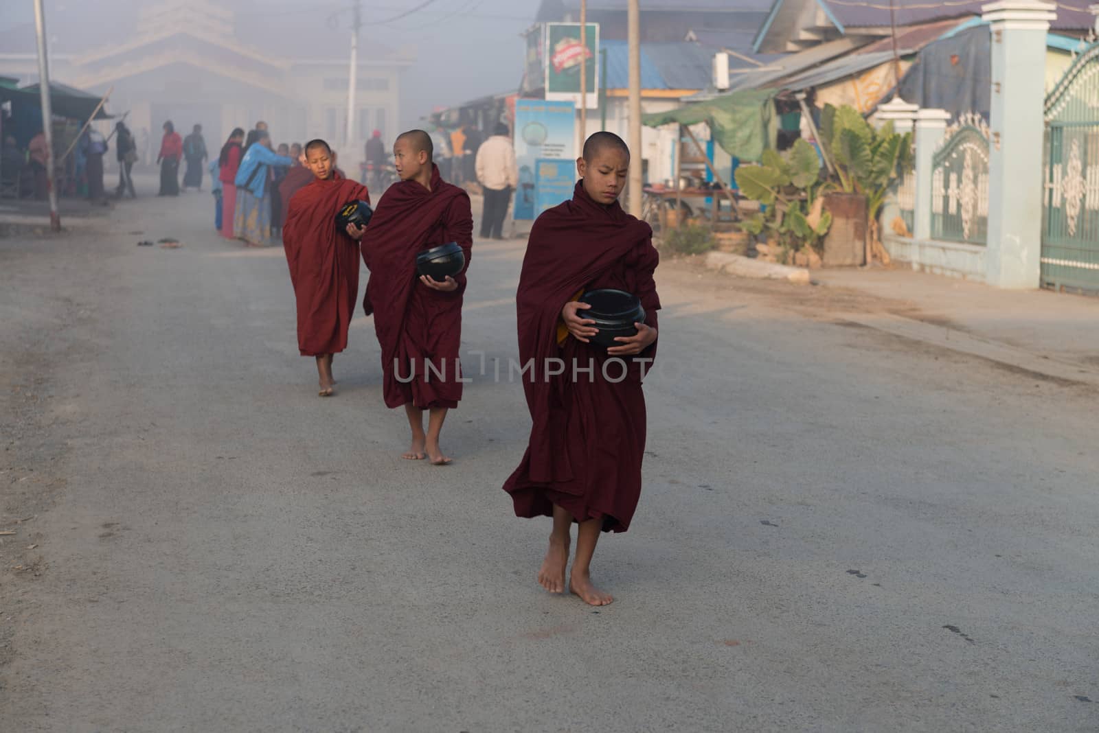 INLE LAKE, MYANMAR - 08 JAN 2014: Young monks gather food on early morning almsround. Offering food is one of the oldest and most common rituals in Buddhism.