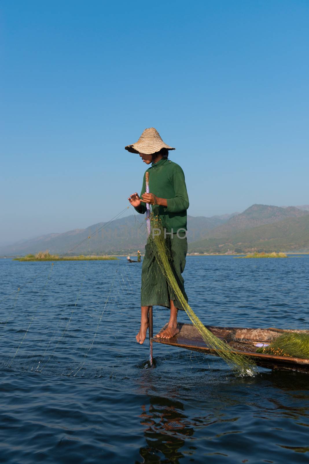 INLE LAKE, MYANMAR (BURMA) - 07 JAN 2014: Burmese fisherman in wooden boat leg row and use net to catch fish in Inle lake, Myanmar