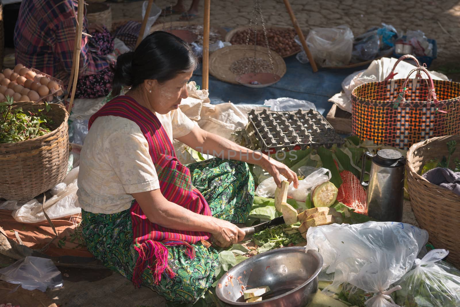 INLE LAKE, MYANMAR (BURMA) - 07 JAN 2014: Local Burmese Intha woman cut and sell vegetable on a traditional open market. Local markets serves most common shopping needs Inle Lake people.