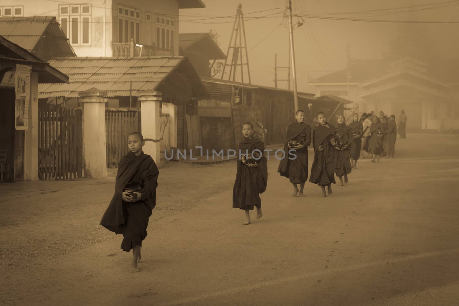 INLE LAKE, MYANMAR - 08 JAN 2014: Young monks gather food on early morning almsround. Offering food is one of the oldest and most common rituals in Buddhism.