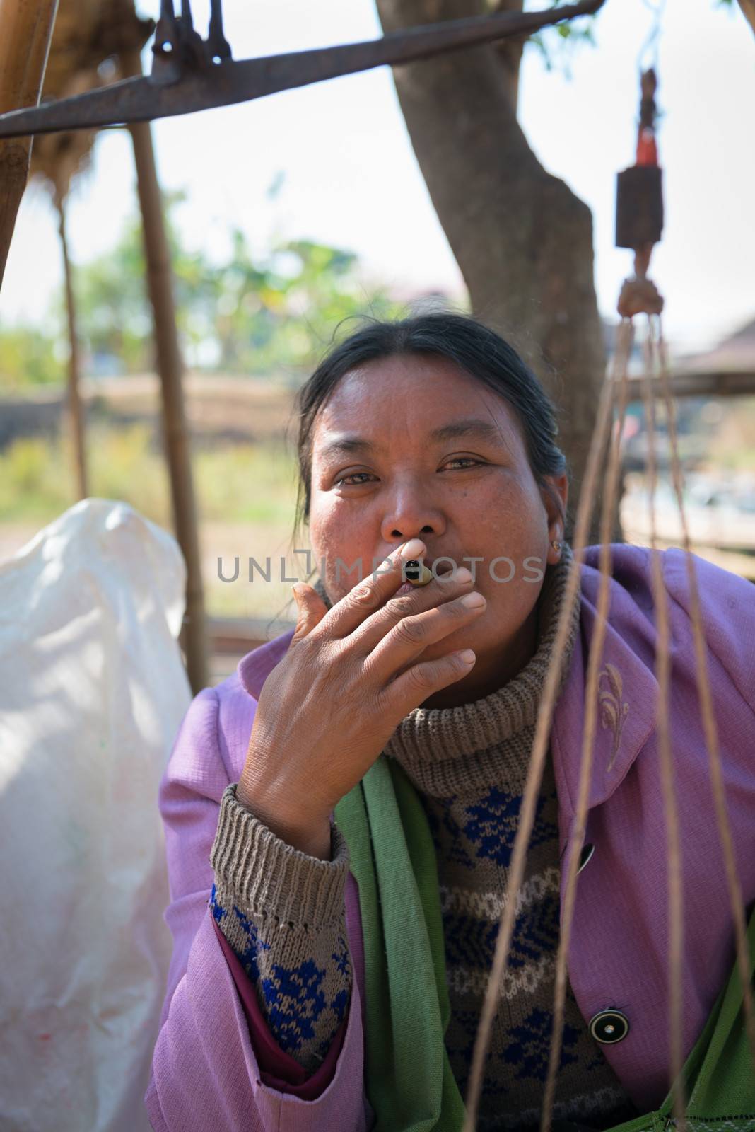 INLE LAKE, MYANMAR (BURMA) - 07 JAN 2014: Local Burmese Intha market woman smoke cheroot cigar with scale details on front. Cheroots are Burmese facial feature.