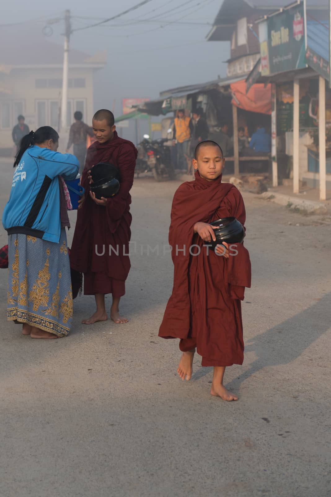 INLE LAKE, MYANMAR - 08 JAN 2014: Young monks gather food on early morning almsround. Offering food is one of the oldest and most common rituals in Buddhism.