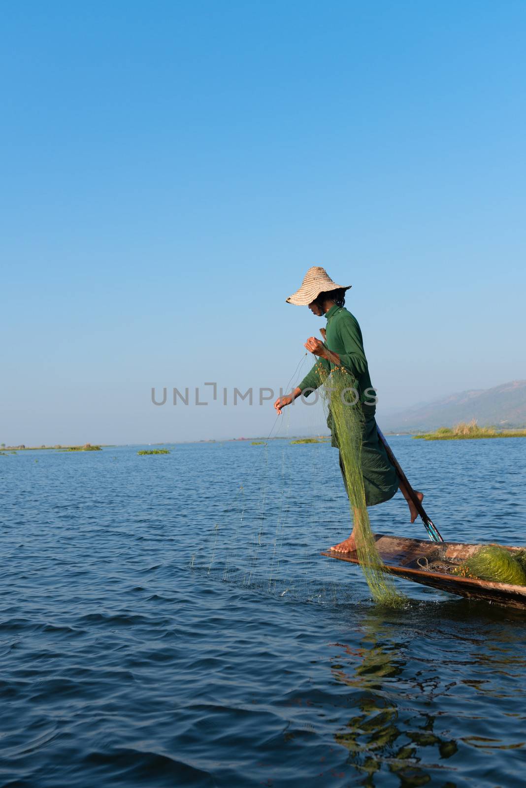 INLE LAKE, MYANMAR (BURMA) - 07 JAN 2014: Burmese fisherman in wooden boat leg row and use net to catch fish in Inle lake, Myanmar