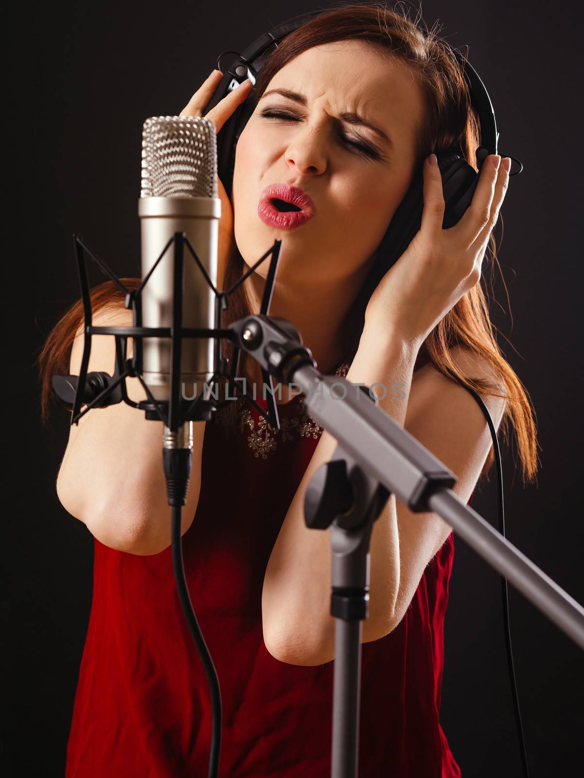 Photo of a beautiful woman singing into a large diaphragm microphone over dark background.