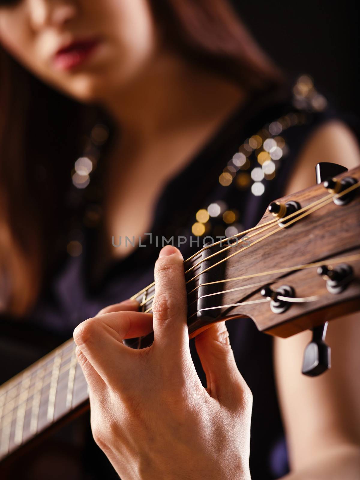 Photo of a woman playing an acoustic guitar with extreme shallow depth of field with focus on hand and headstock.