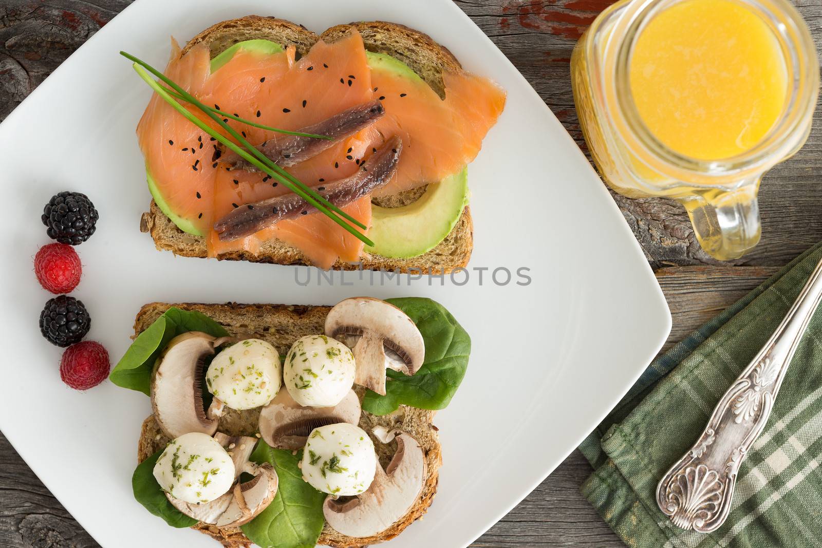 Overhead view of a plateful of healthy picnic snacks with freshly squeezed orange juice with two open sandwiches with smoked salmon, avocado, mushrooms and mozzarella cheese