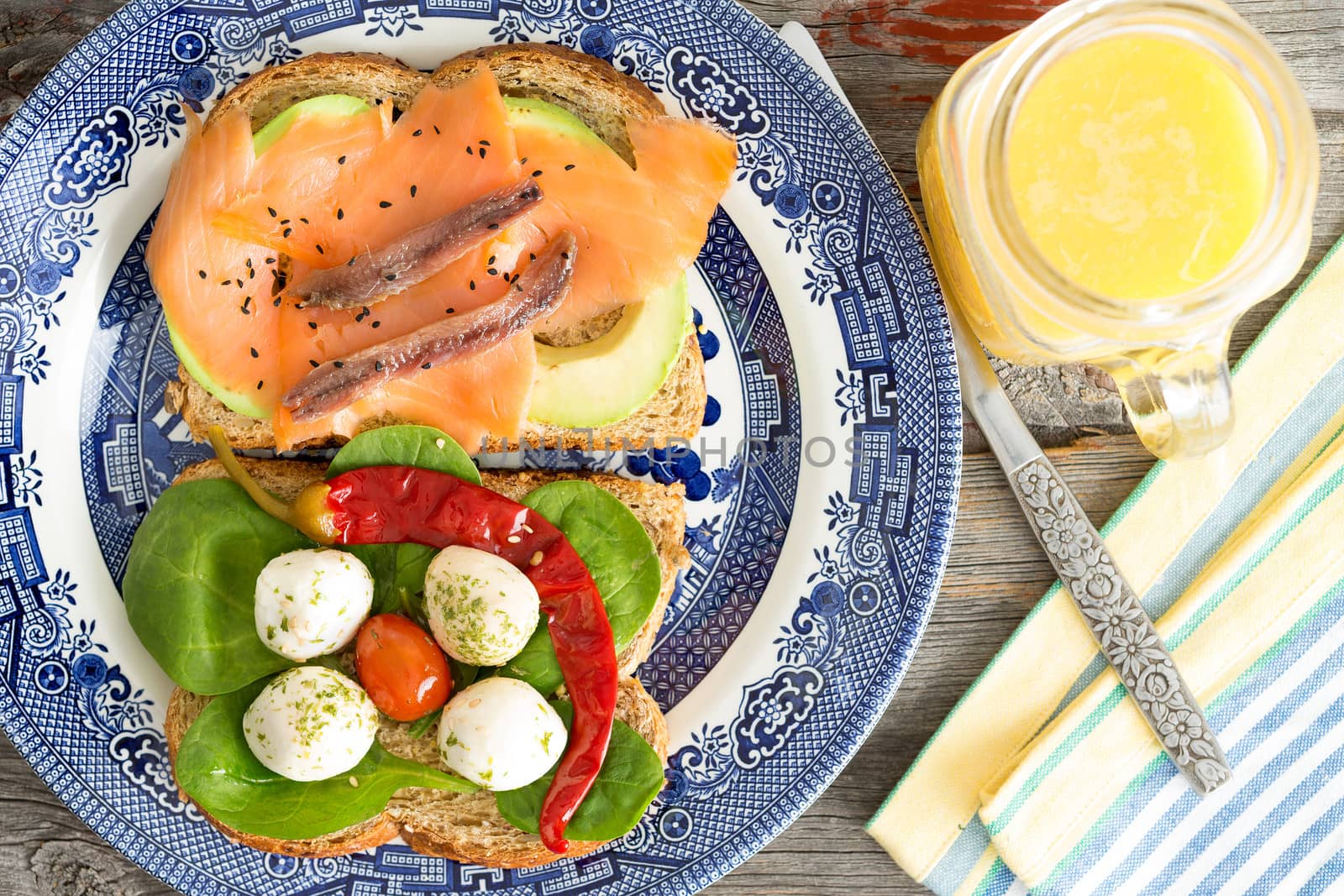 Healthy gourmet picnic lunch with a serving of smoked salmon, avocado, mozzarella cheese, jalapeno pepper and baby spinach on wholewheat bread accompanied by a jug of fresh orange juice, overhead view