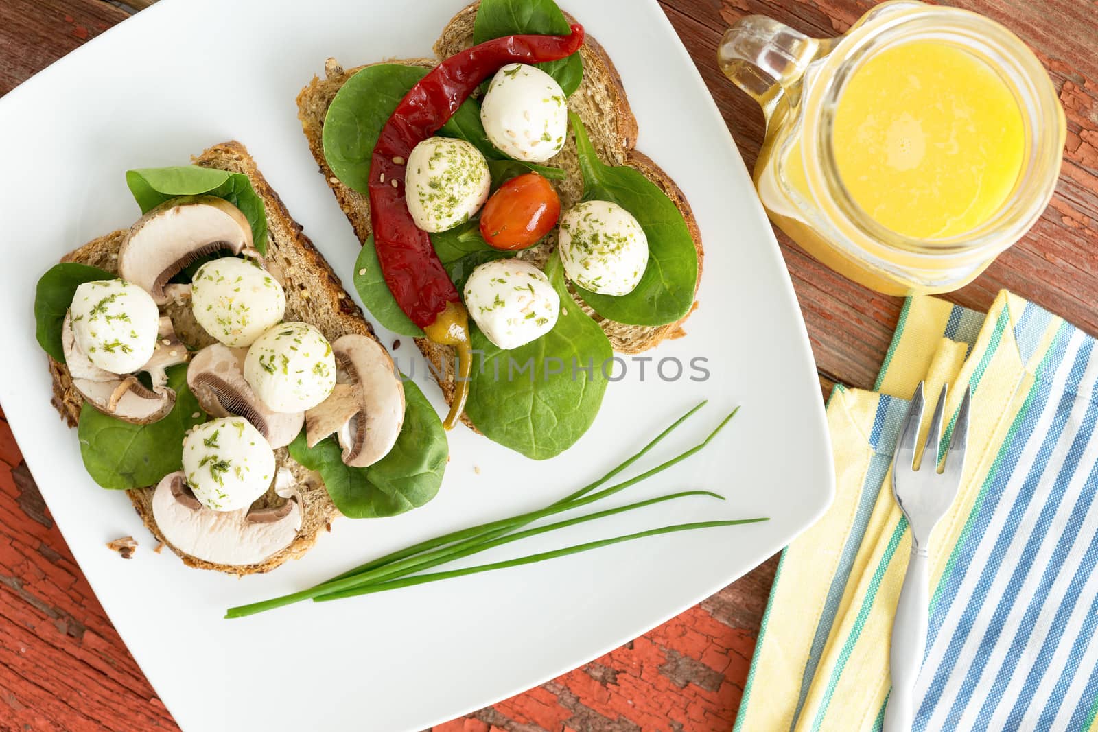 Wholesome healthy picnic lunch with delicious wholewheat bread topped with fresh baby spinach, mozzarella cheese, hot chili pepper, and mushrooms served with a jug of freshly squeezed orange juice