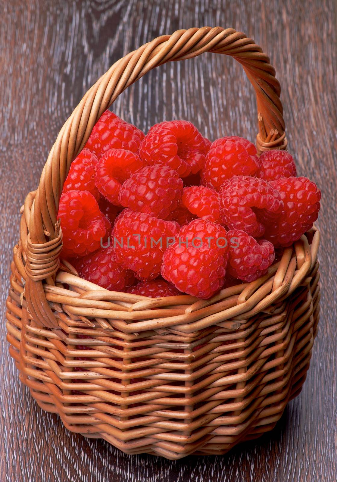 Fresh Ripe Raspberries into Wicker Basket closeup on Wooden background