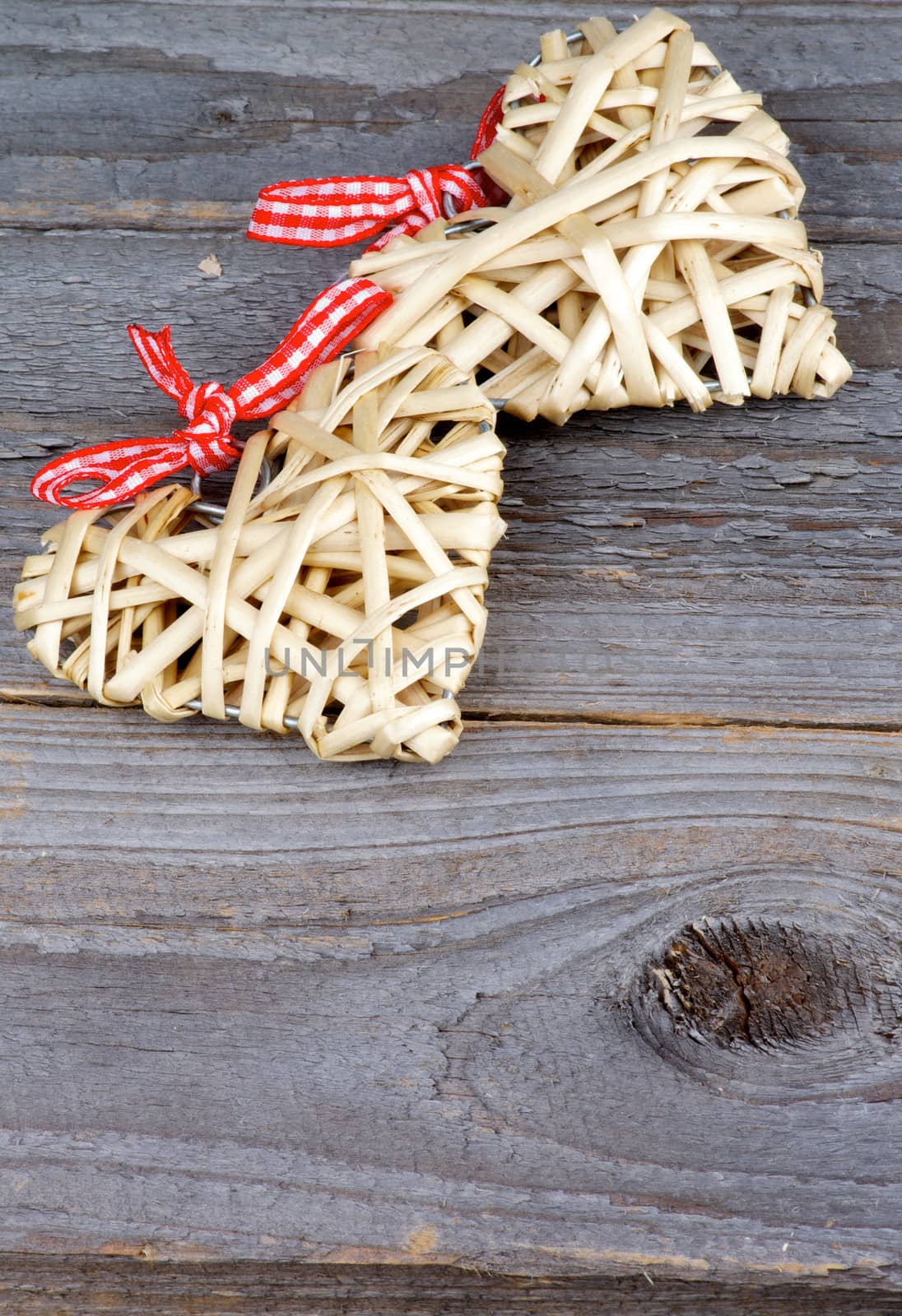 Two Handmade Wicker Hearts with Red Checkered Bows isolated on Rustic Wood background