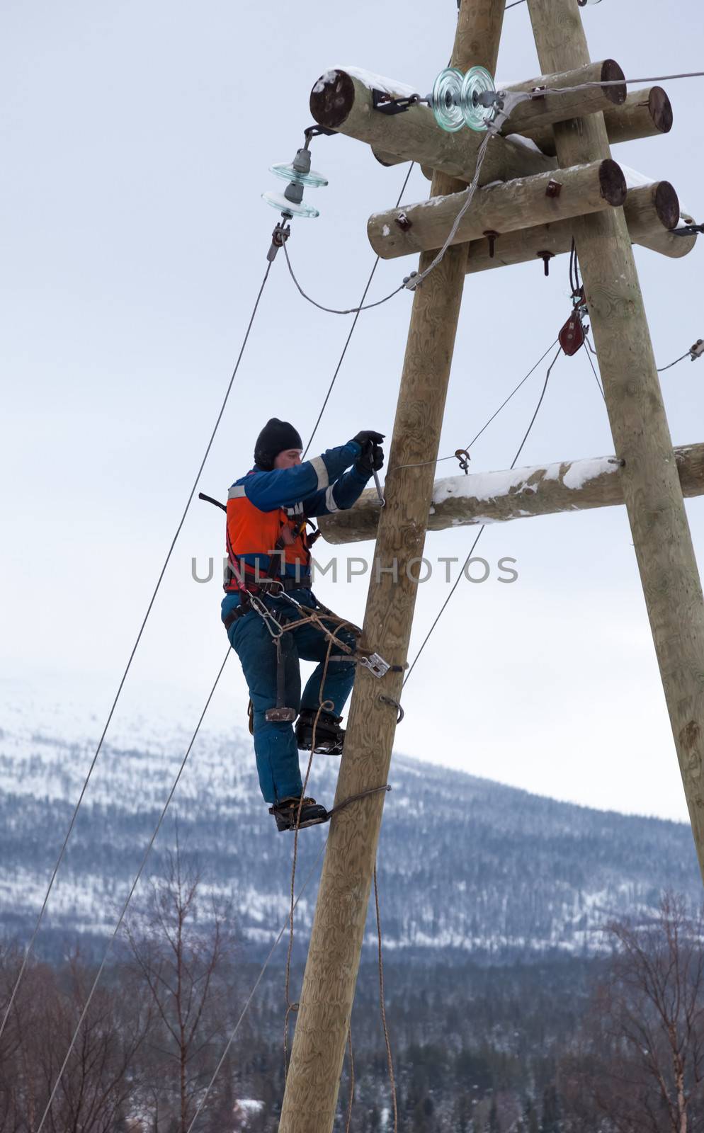 Electricians working on a pole in winter with the use of claws-manholes and belt 