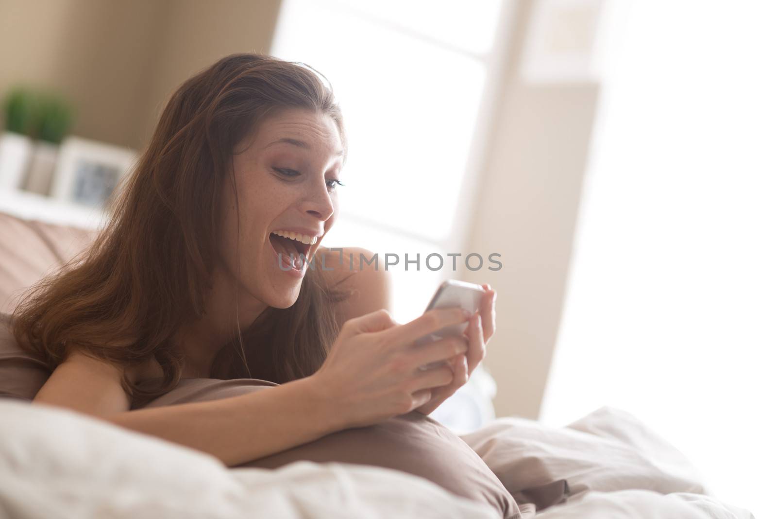 Happy woman at home reading a text message in her bright bedroom 