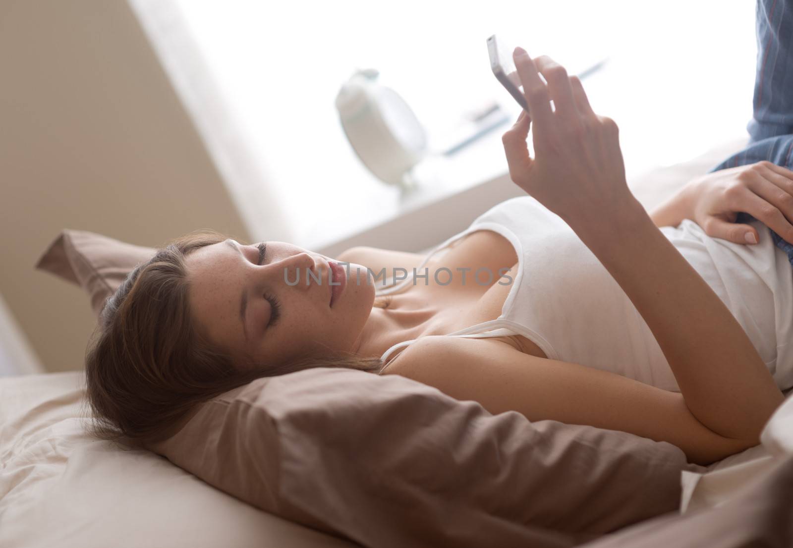 Young woman lying on the bed at home and receiving a text 