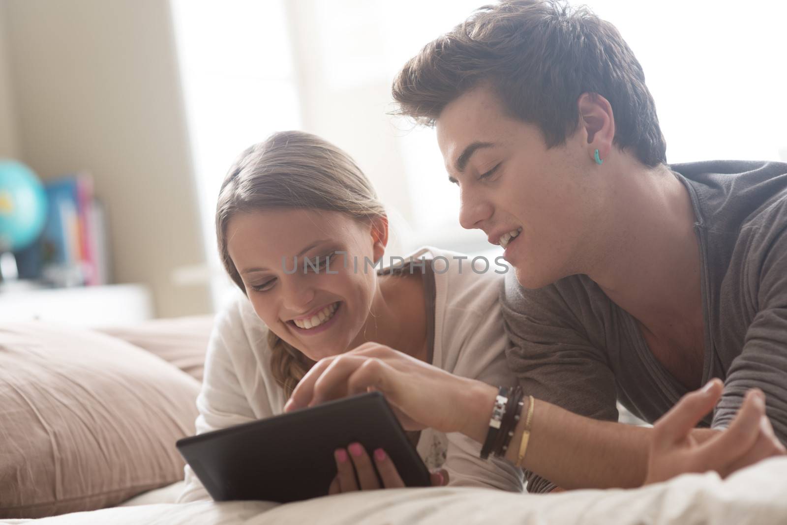 Two happy friends lying in bed using a digital tablet together 