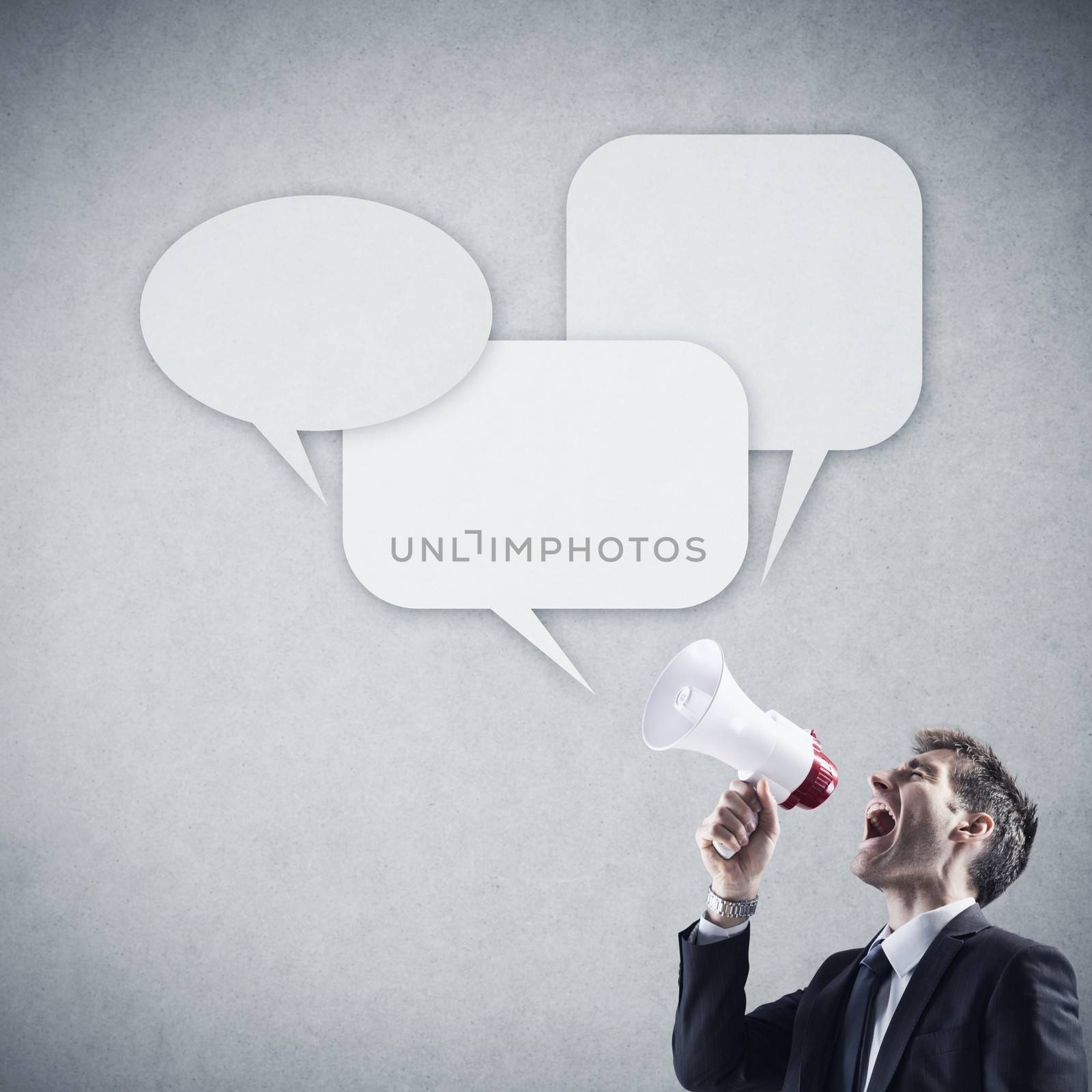 Angry young businessman shouting into megaphone against grey background 