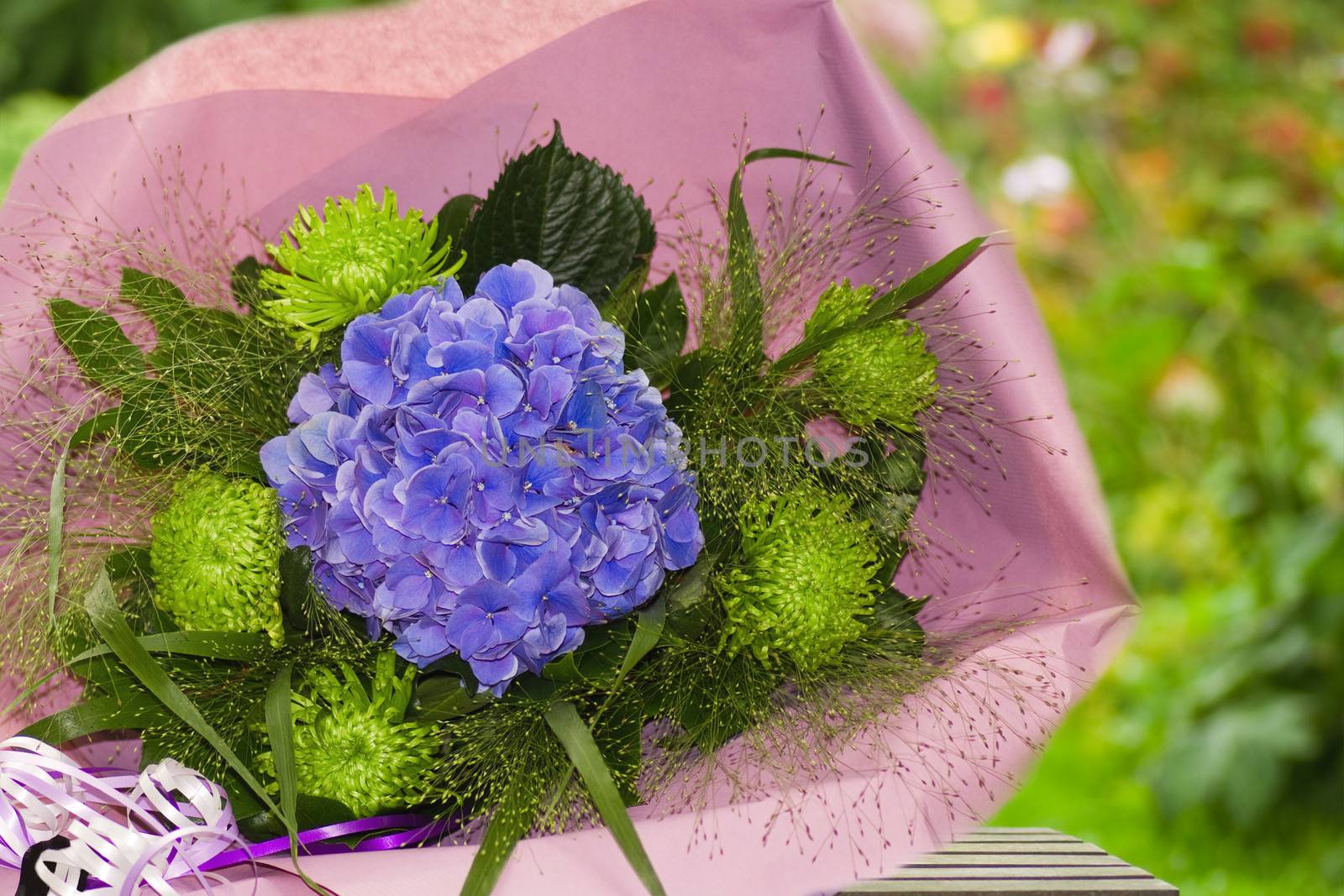 Blue and green bouquet of flowers wrapped in paper with summer garden background