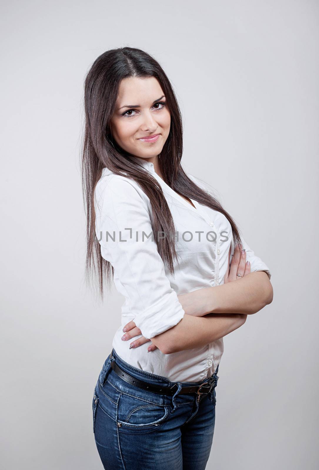 Beautiful young businesswoman standing with hands folded. Studio shot over gray background.