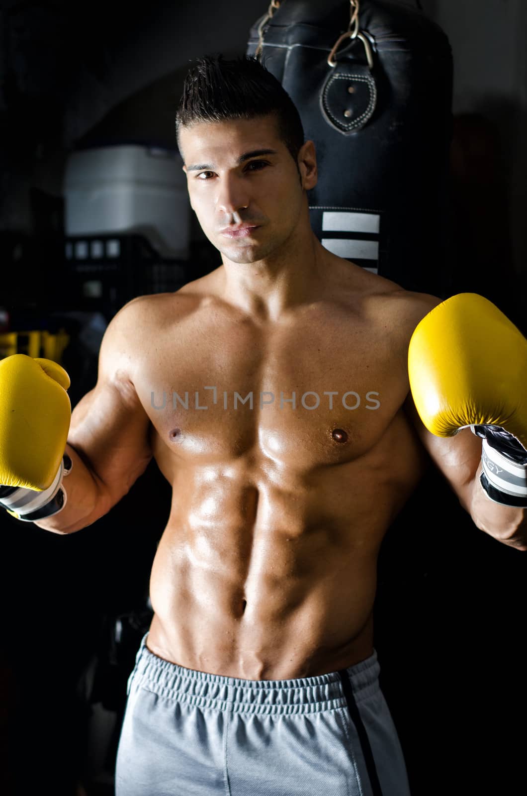 Handsome shirtless and muscular young man with boxer's gloves in a gym