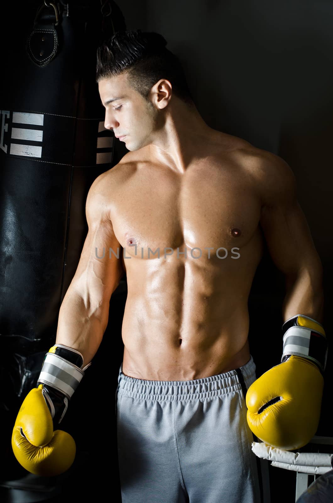 Handsome shirtless young man with boxer's gloves in a gym