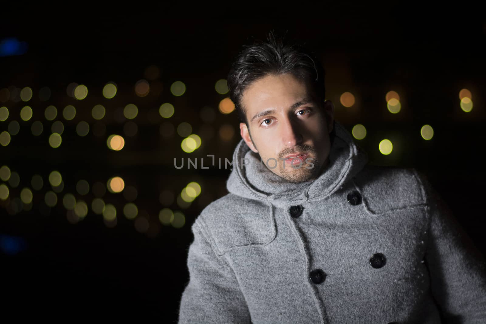 Attractive young man portrait at night with city lights behind him, looking at camera