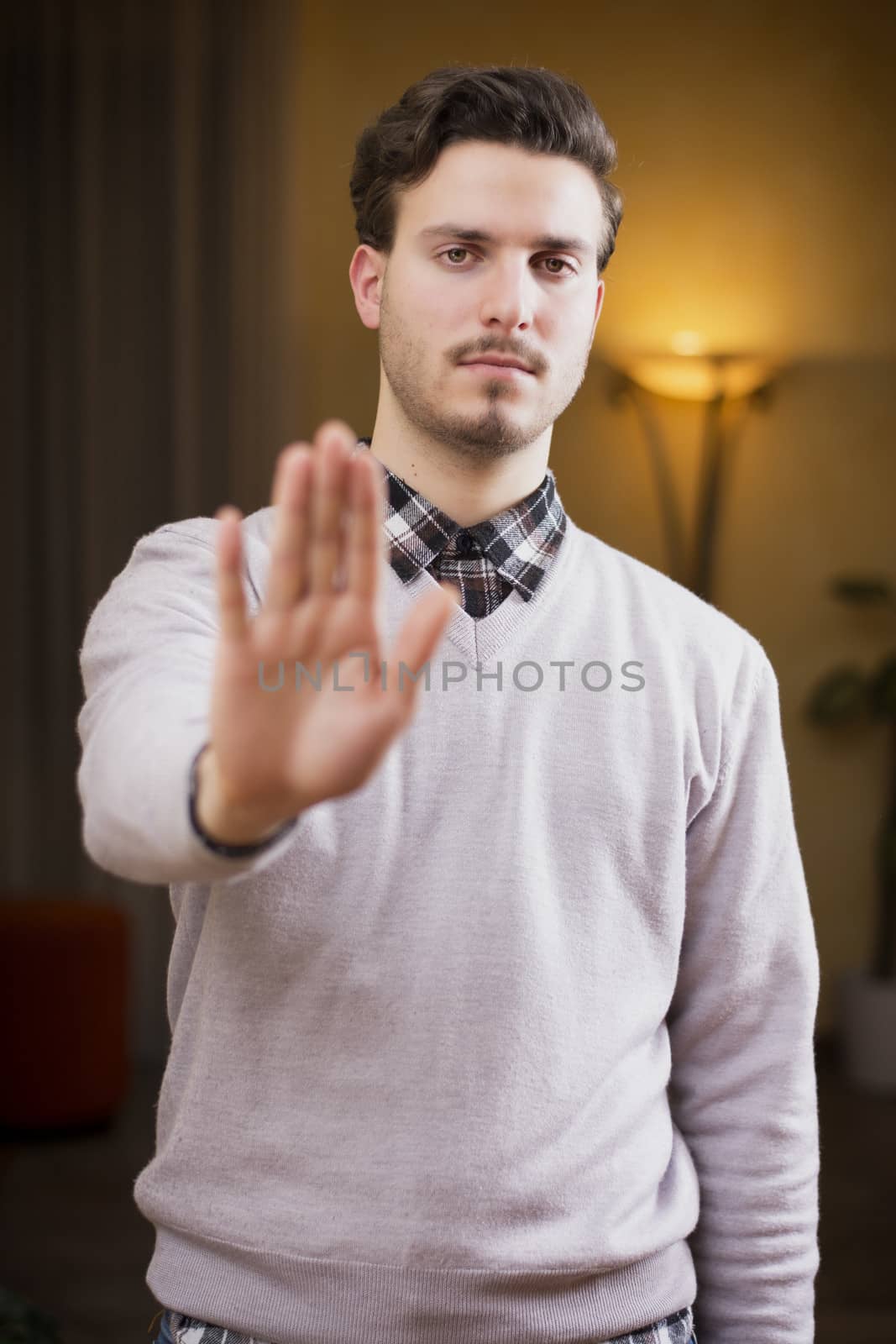 Handsome, seerious young man doing stop sign with his hand with a severe expression. 