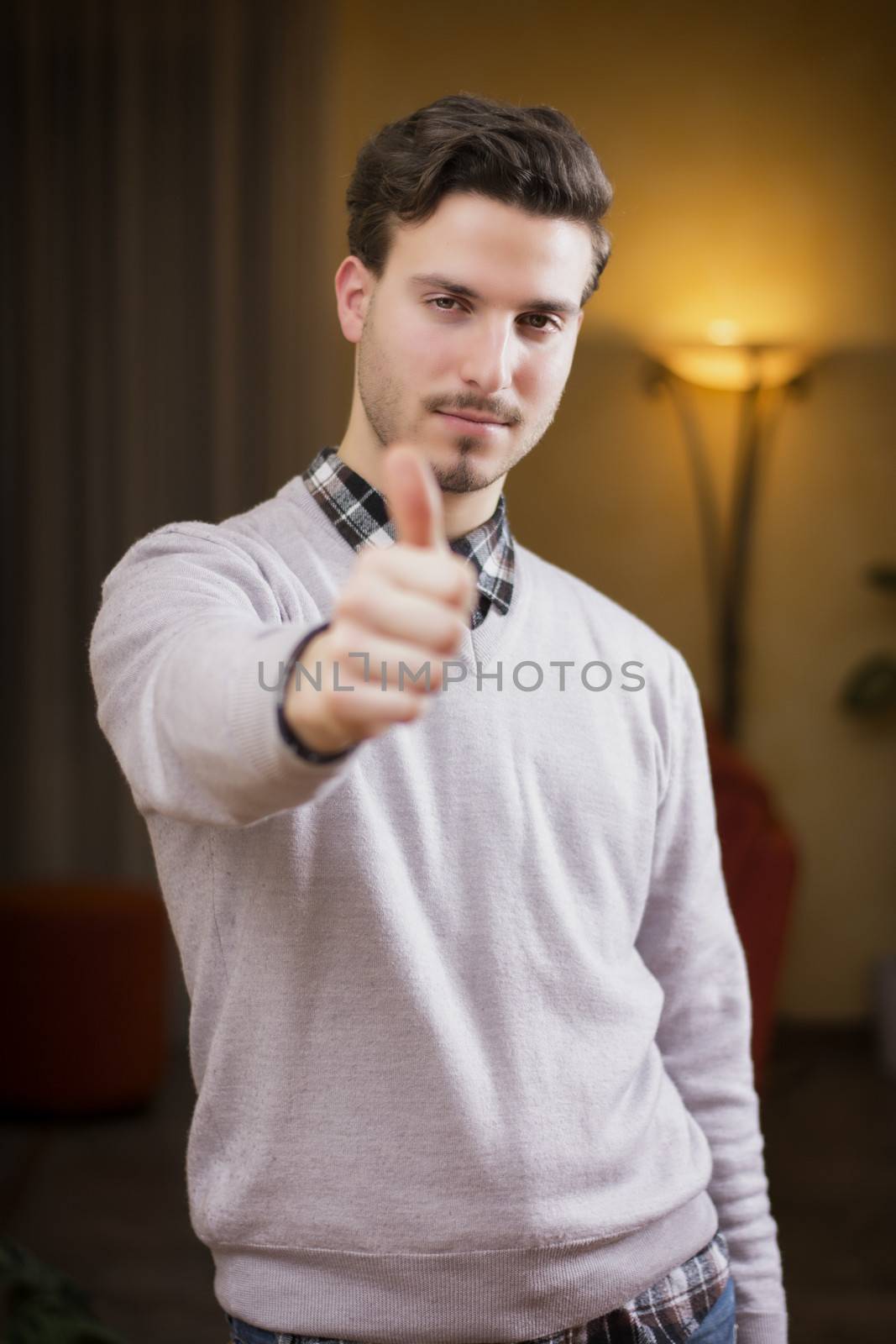 Attractive young man with thumb up doing OK sign, indoor shot inside a house