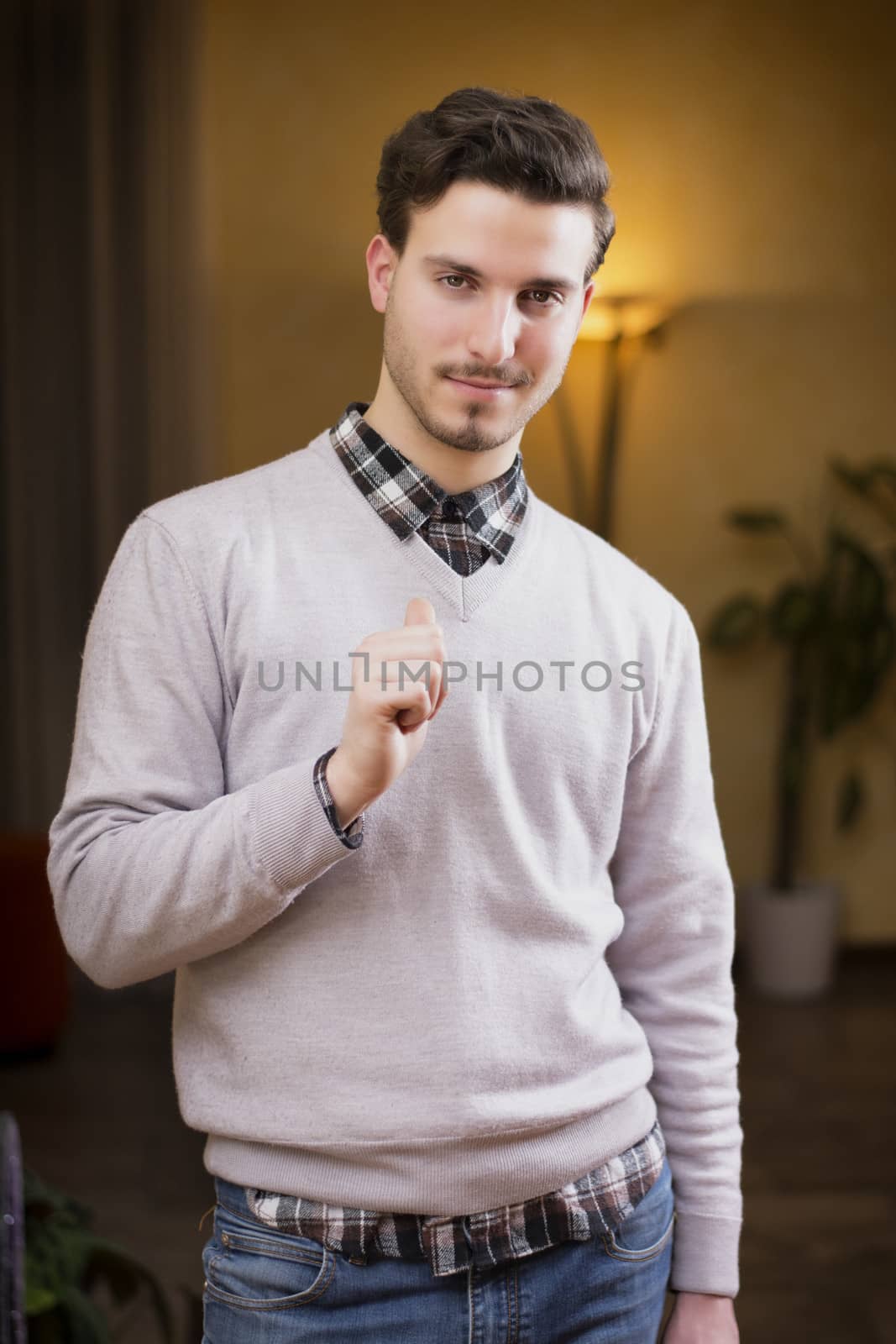 Handsome young man pointing finger at himself, smiling. Indoors shot inside a house