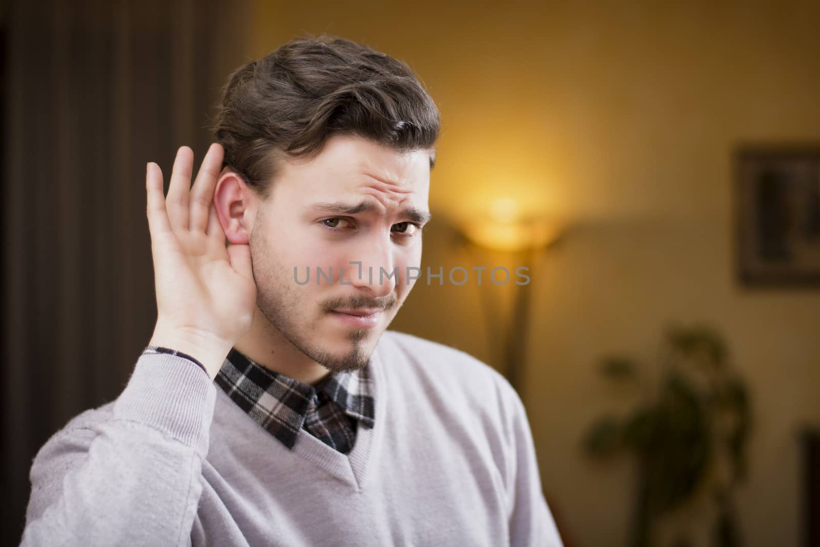 Handsome young man can't hear, putting hand around his ear. Indoors shot inside a house