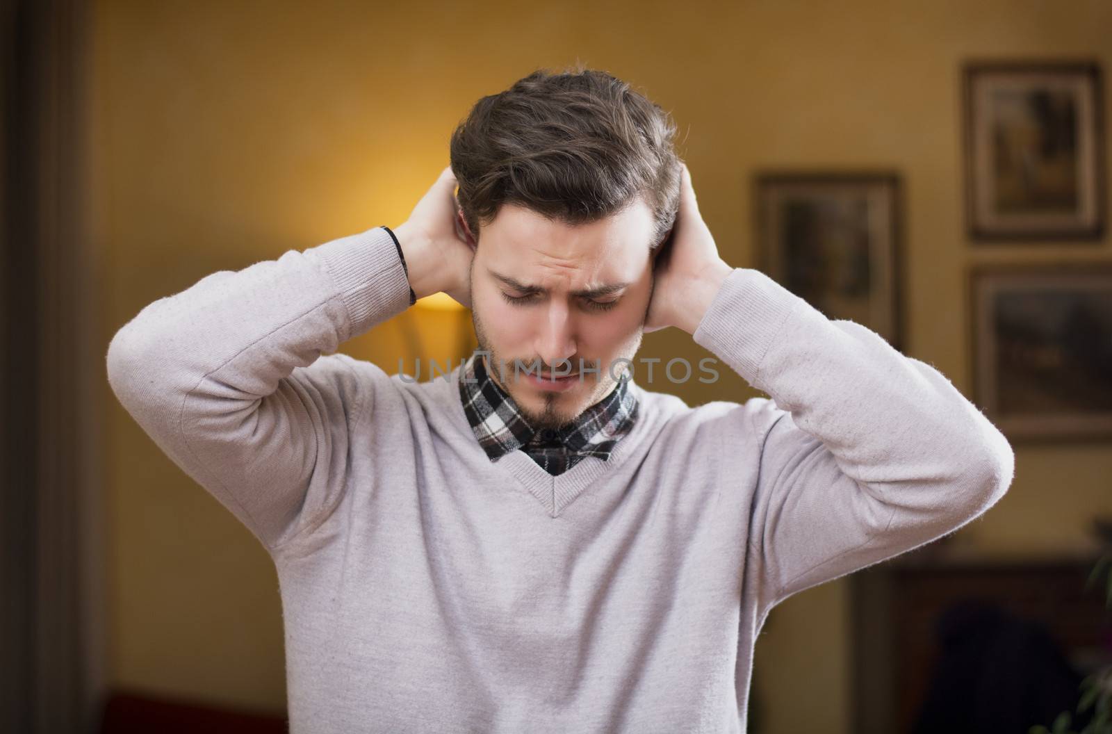 Handsome young man covering his ears, stressed or unhappy because of too much noise. Indoors shot