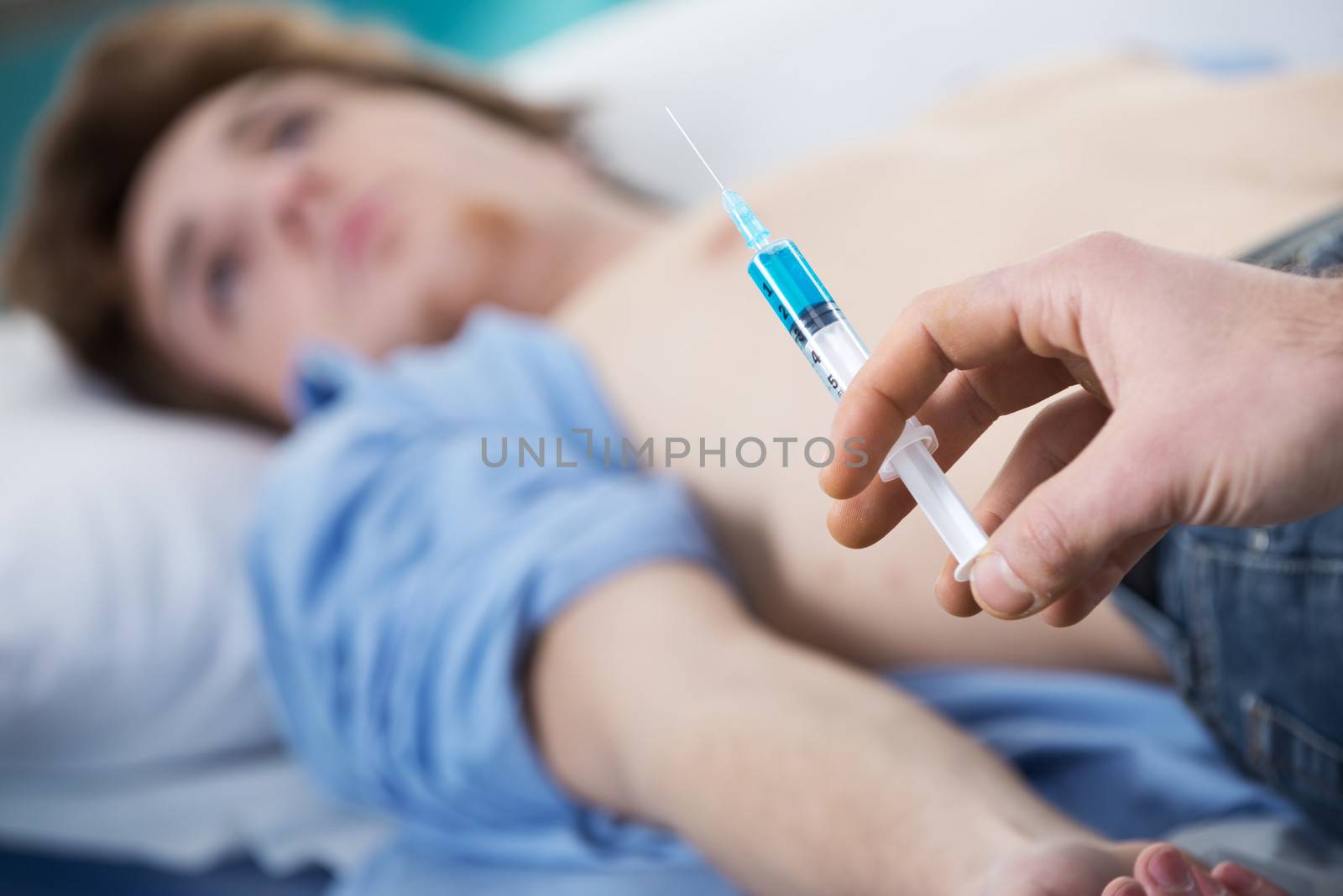 Doctor preparing a syringe for an injection with patient on the background.