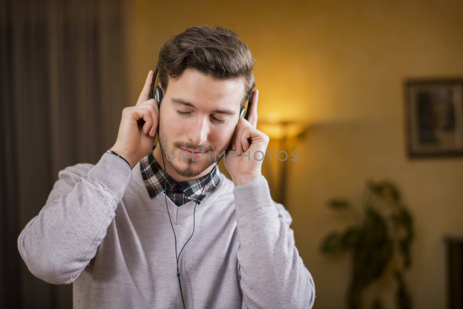 Attractive young man listening to music on headphones, eyes closed. Indoor shot in house