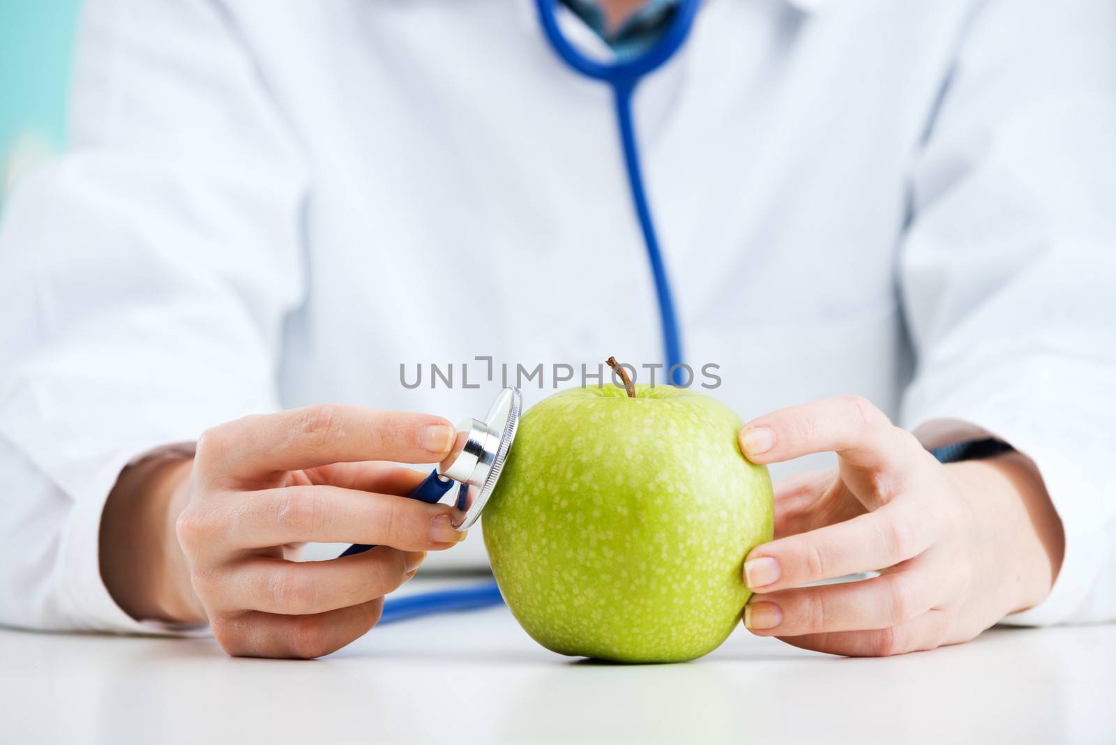Female doctor uses her stethescope to check the health of an apple 