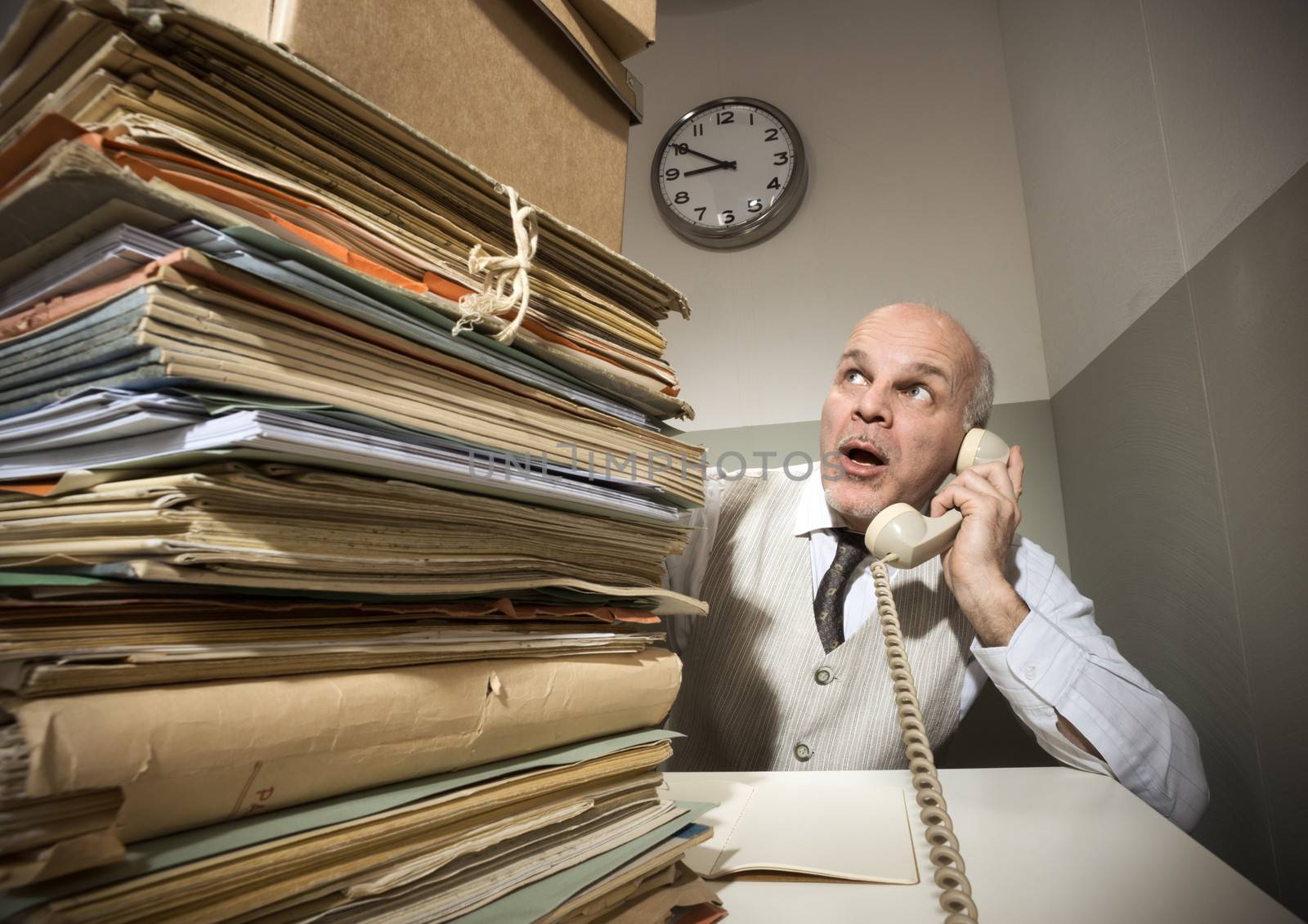 Vintage senior businessman on the phone with a huge stack of files.