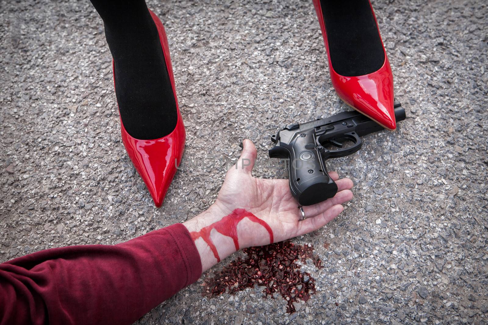 Man is dominated by a woman with red shoes, the shoe tread gun arm bloodied on the asphalt