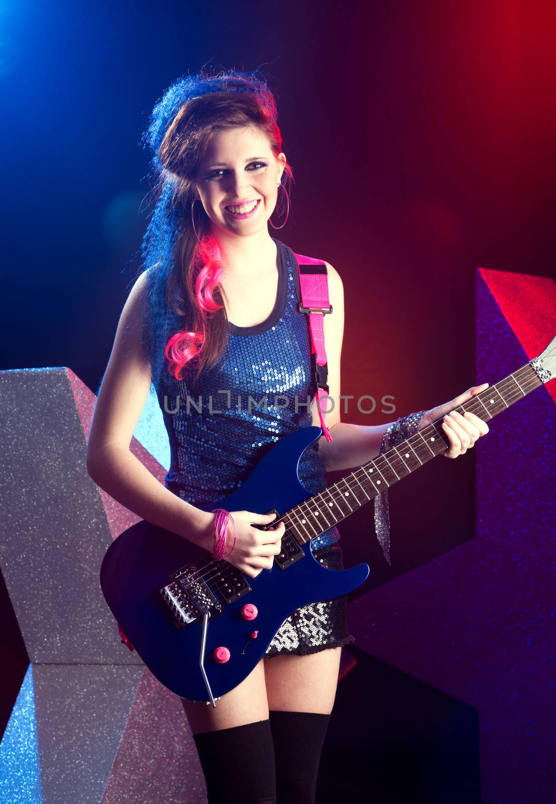 Young teenager rock star singing and playing electric guitar on stage.