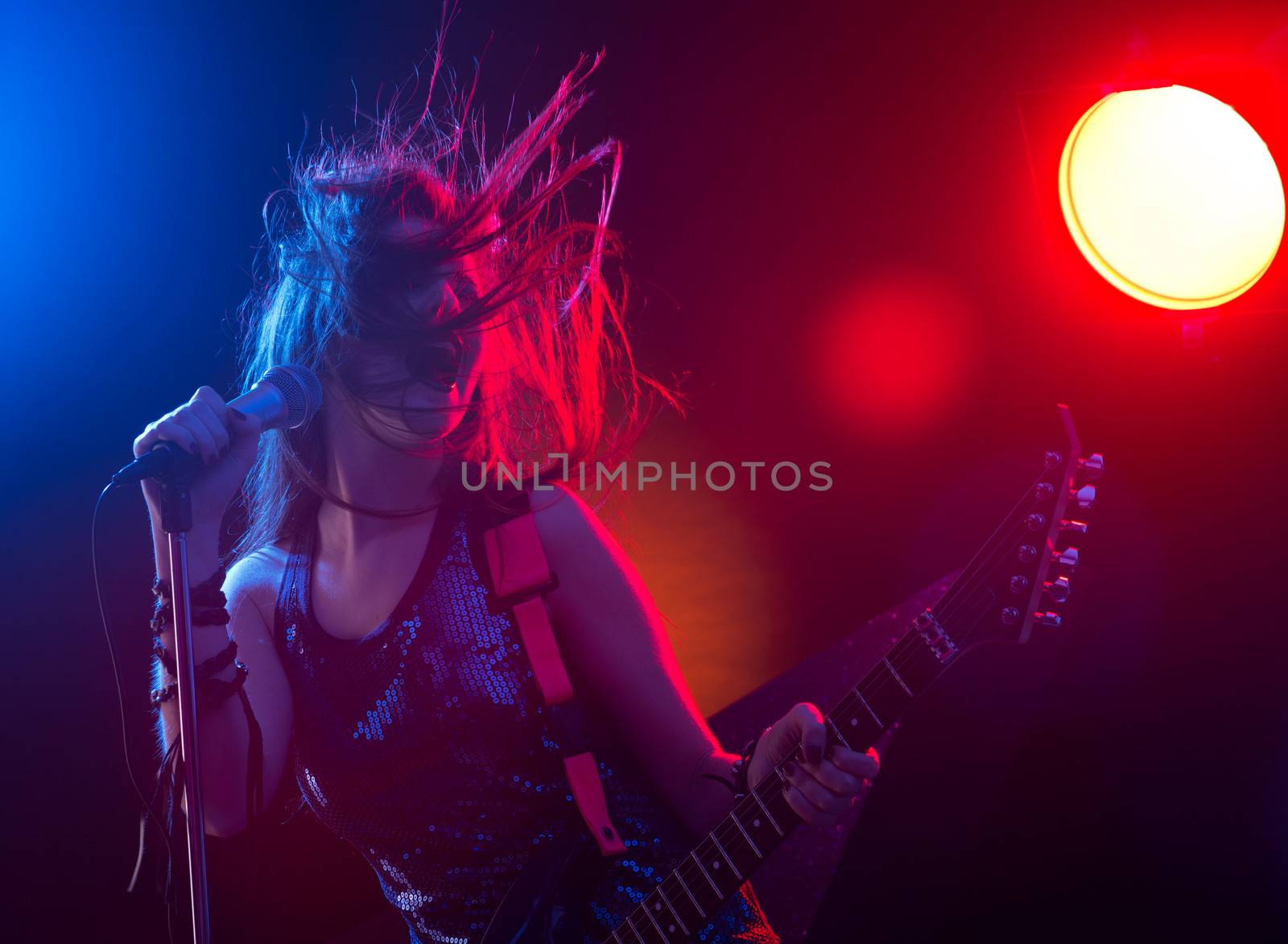 Young teenager rock star singing and playing electric guitar on stage.