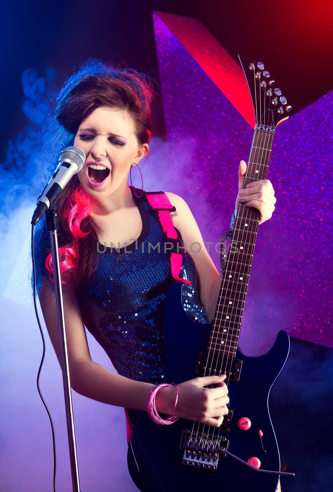 Young teenager rock star singing and playing electric guitar on stage.
