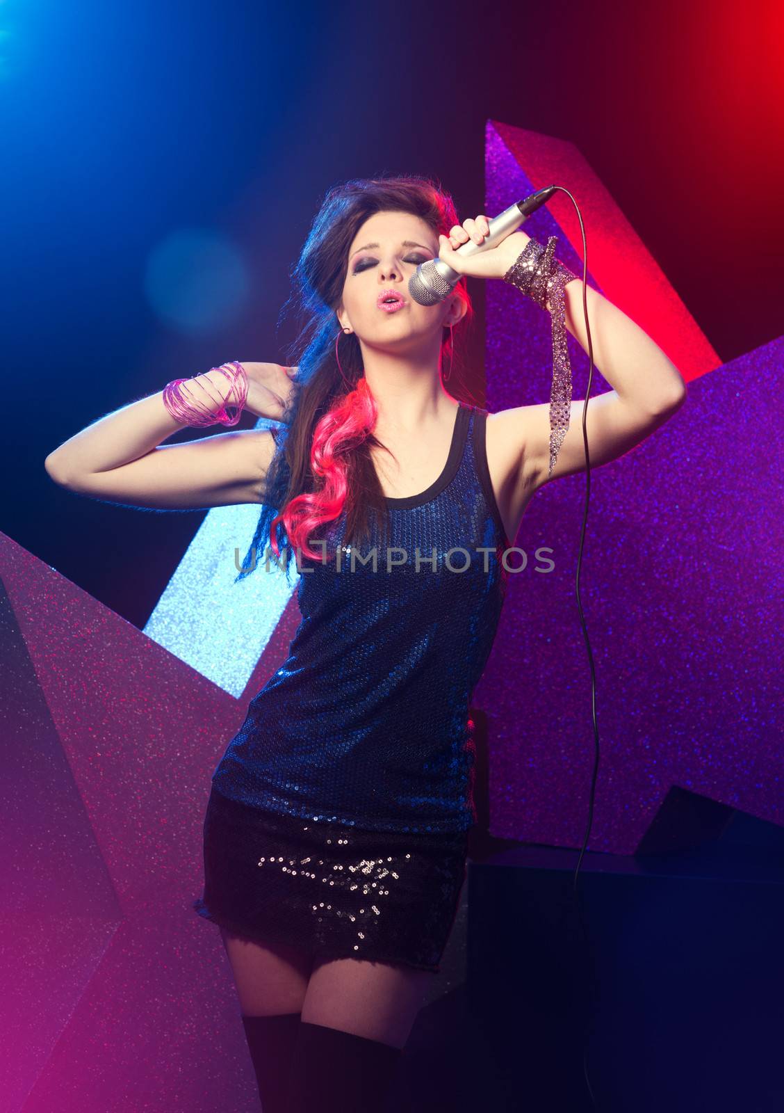 Young beautiful girl singing on stage with star on background.