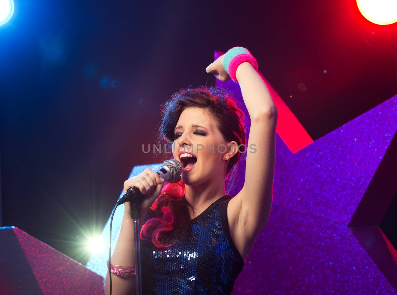 Young beautiful girl singing on stage with star on background.