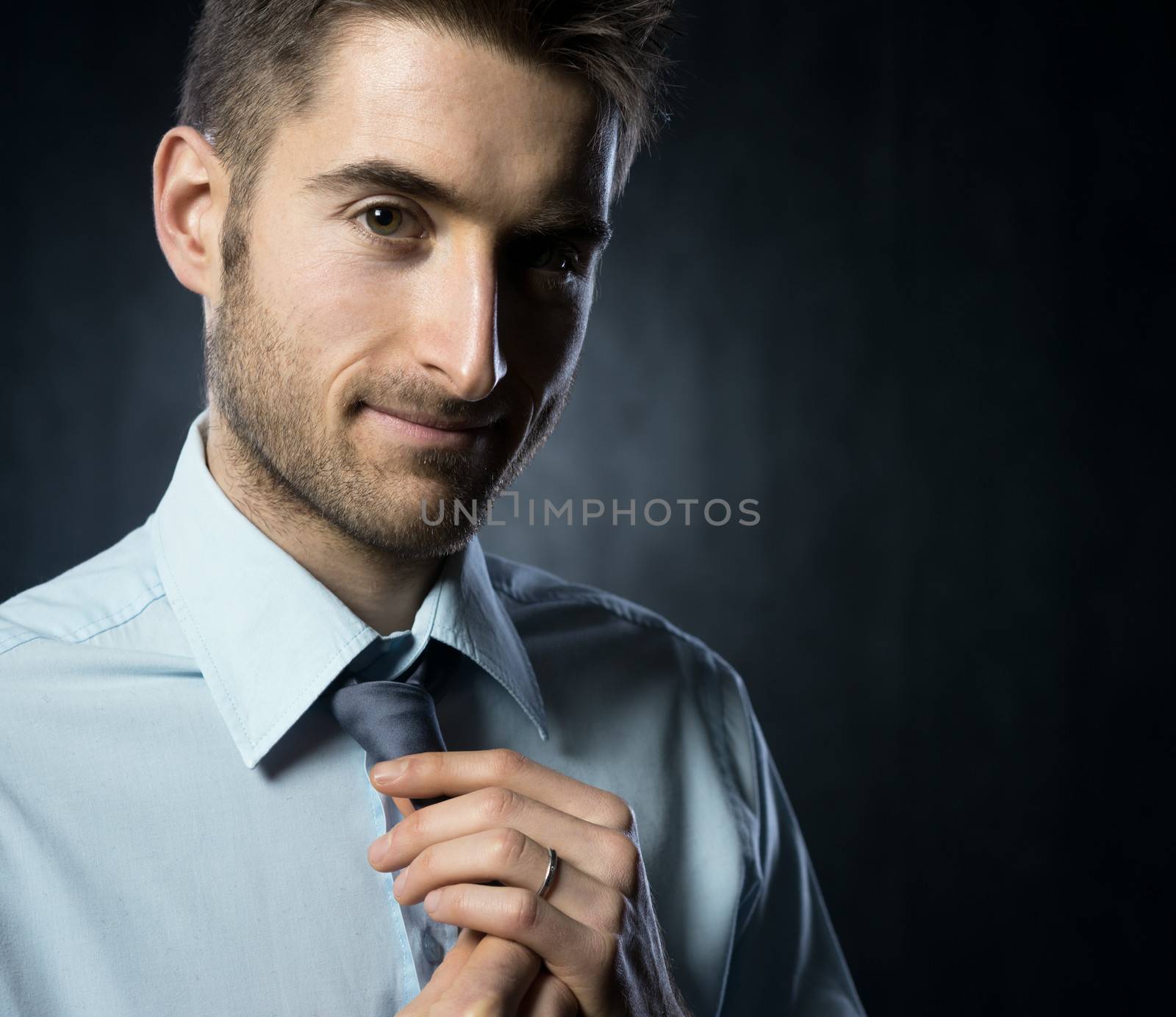 Young elegant man adjusting tie knot and smiling.