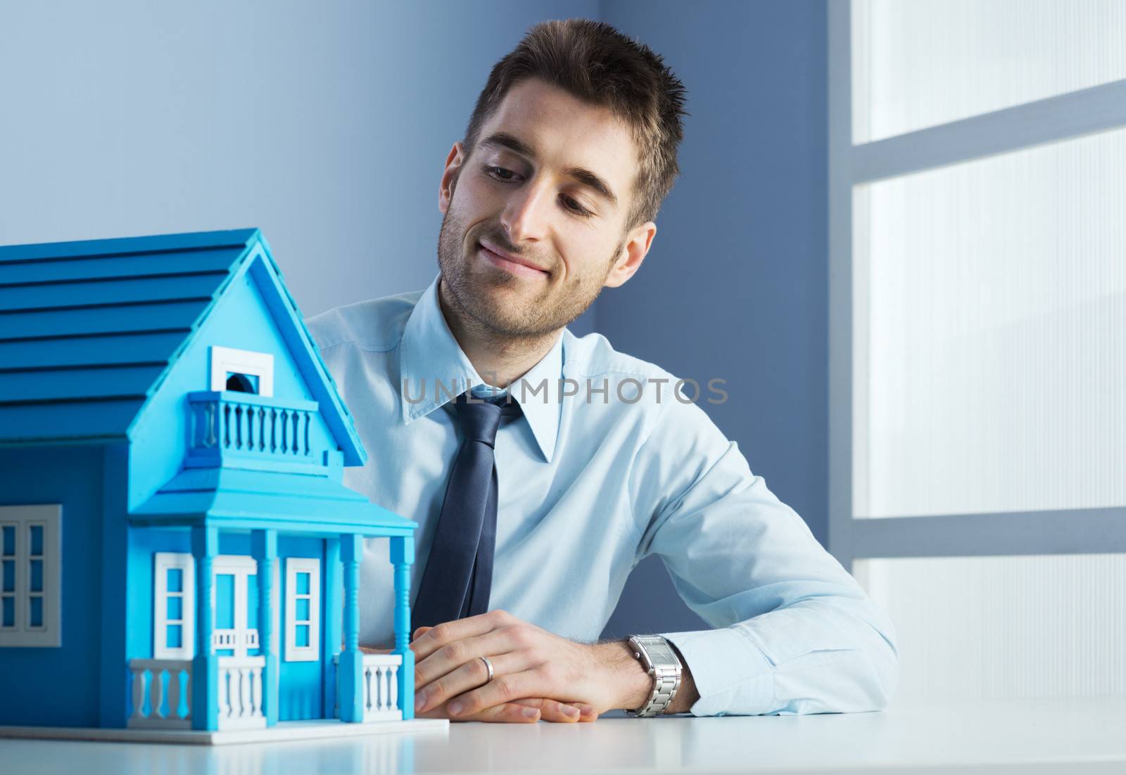 Friendly real estate agent with light blue model house.