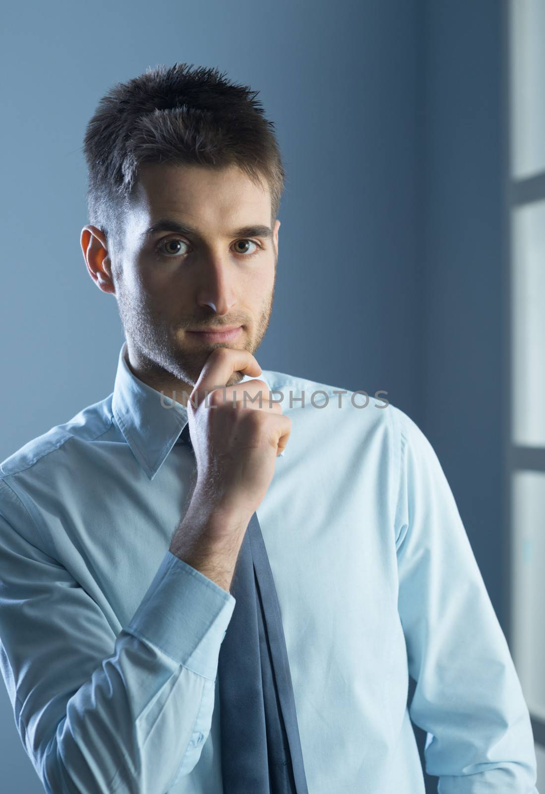 Young businessman with hand on chin, looking at camera.