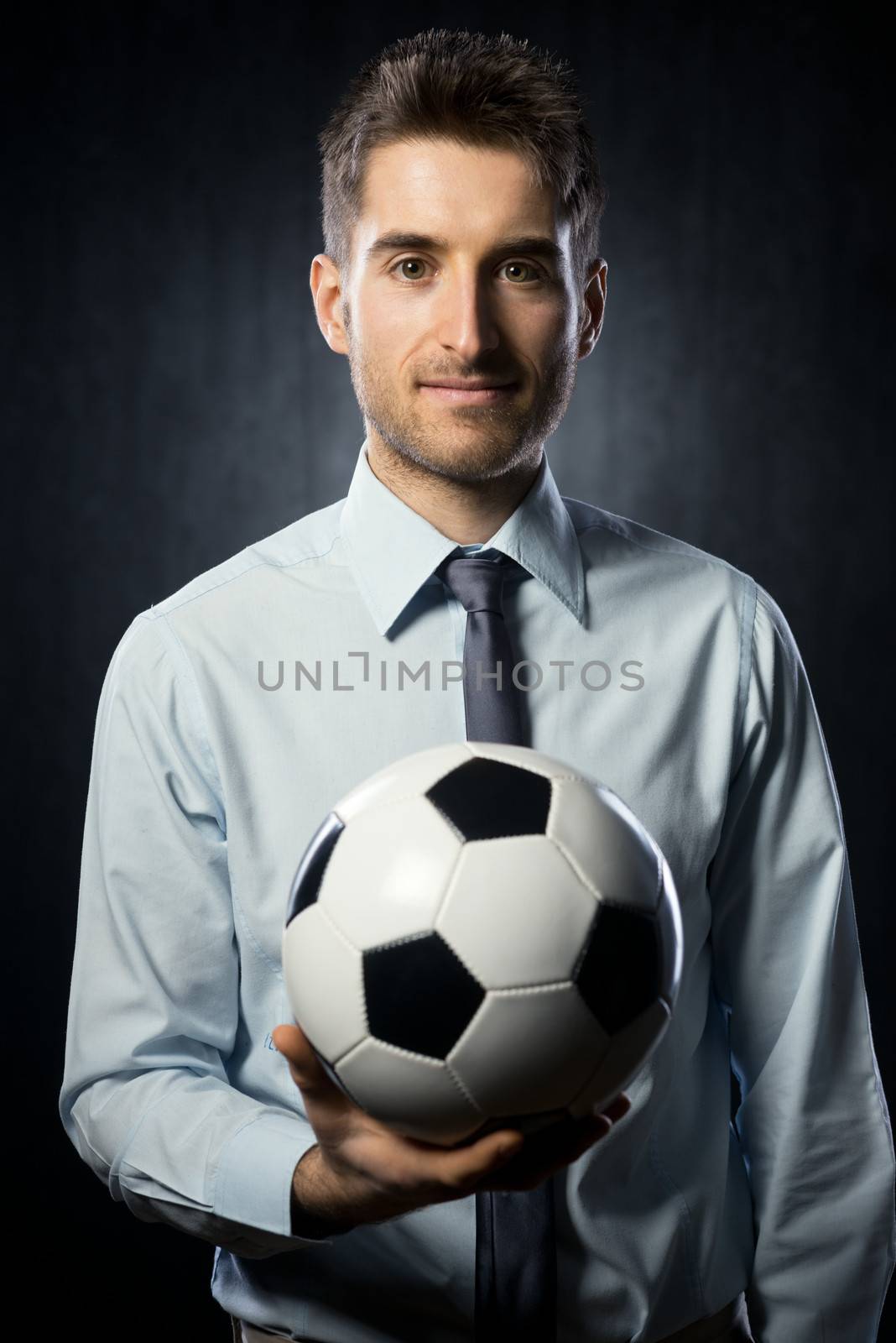 Young attractive businessman holding a soccer ball and smiling.